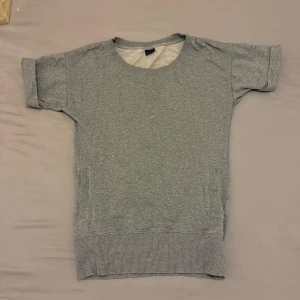 Grå lång topp - Snygg grå lång topp med korta ärmar och ribbad nederkant. Perfekt för en avslappnad stil.