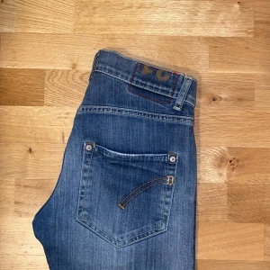 Blå jeans från Dondup - Snygga blå jeans från Dondup med klassisk femficksdesign och knappgylf. Tillverkade i Italien, dessa jeans har en stilren look med subtila slitningar och kontrastsömmar. Perfekta för en avslappnad stil. Storlek 31 med utmärkt skick! Först till kvarn.
