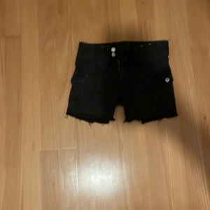 Svarta jeansshorts - Säljer ett par svarta jeansshorts med fransiga kanter och knappar framtill. De var först ett par jeans men jag klippte de och de blev för korta för min smak