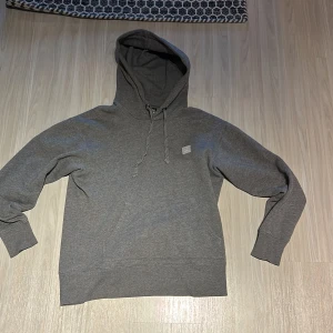 Grå hoodie från Acne Studios - Säljer en stilren grå hoodie från Acne Studios. Tröjan har en klassisk design med justerbar huva och en liten logotyp på bröstet. Köpte tröjan för ungerfär 2500kr. Hör av er av minsta fundering :)