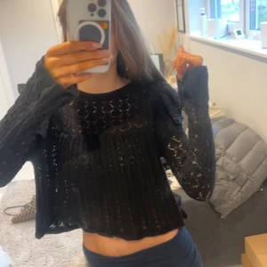 Svart stickad croppad tröja - Säljer en svart stickad tröja med ett snyggt hålmönster. Tröjan är croppad och har långa ärmar, perfekt för en trendig look. Passar bra till både jeans och kjol.