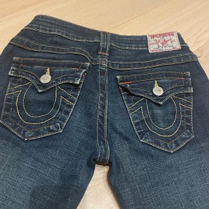 Mörkblå jeans från True Religion - Snygga mörkblå jeans från True Religion i storlek 26. De är väldigt lowaisted och sitter jättefint på! Jag köpte dem för 1200kr men säljer för 1000kr , men pris kan diskuteras. Jag är 158 cm och de är lite långa på mig men funkar med skor.Skulle rekommendera till någon som är runt 165 cm. Om du vill ha fler bilder är det bara att skriva 💗Har även lite slitage på ett av bene men absolut inget märkbart!☺️