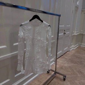 Vit studentklänning  med blommigt mönster och öppen rygg - Jättefin mönstrad klänning perfekt till studenten. Klänningen är öppen i ryggen.