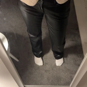 Svarta byxor i syntetmaterial - Snygga svarta byxor i syntetmaterial med en stilren design. Perfekta för en trendig look. Byxorna har en normal passform och är midwaist. Plagget har även inte används💛