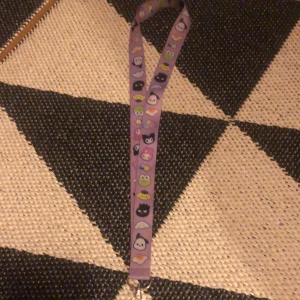 Sanrio nyckelband - Jag säljer ett ljuslila nyckelband med sanrio karaktärer på!! Defekter: liten blå fläck och en del av ”nyckelhållaren” är borta. Den är köpt på comic con för 100kr!!