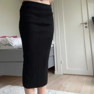 Svart ribbad kjol - Snygg svart ribbad kjol i midi-längd. Perfekt för en stilren look med en tight passform som framhäver figuren. Kjolen är enkel att matcha med olika toppar och accessoarer.