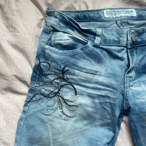 Blå jeans med feta detaljer   - Snygga lågmidjade ljusblå jeans från Eleven med unikt broderi och strassdetaljer på fram- och baksida. Jeansen är straight leg men är också lite stretchiga. Några stenar saknas men det syns inte på håll och jeansen har tvär snygg knapp och dragkedjor. 