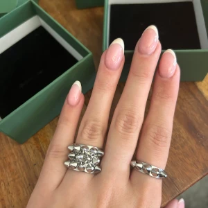 Silvriga ringar med nitar från Edblad - Säljer två supercoola silvriga ringar från Edblad. Den ena ringen har en rad med spetsiga nitar som ger en edgy look, medan den andra har tre rader med nitar för en ännu mer iögonfallande stil. Perfekta för att ge din outfit en tuff touch!