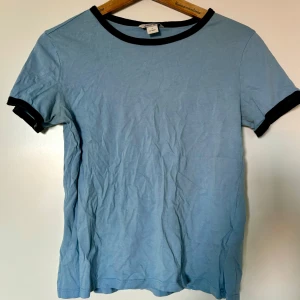 Blå t-shirt med svarta detaljer - Kortärmad t-shirt i ett mjukt material. Sparsamt använd. 
