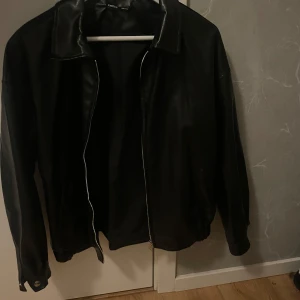 Svart skinnjacka med dragkedja - Säljer en stilren svart skinnjacka med dragkedja framtill. Jackan har en klassisk krage och långa ärmar. Perfekt för höst och vår när du vill ha en cool look. Passar både till vardags och fest!