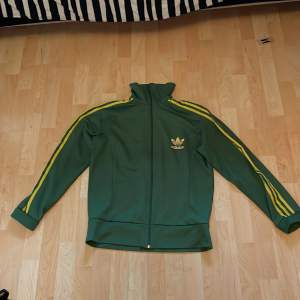 Grön och gul Adidas Tracksuit jacka/hoodie, I fint skick. Storlek XL. Passar mig som M. Skriv om ni har några frågor eller funderingar!