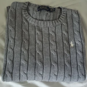 Grå stickad tröja från Ralph Lauren - Säljer en superfin grå stickad tröja från Ralph Lauren efterssom den är för liten för mig . Den har ett klassiskt flätmönster och är i nyskick. Tröjan är långärmad och perfekt för både höst och vinterl. Perfekt för en stilren och mysig look!