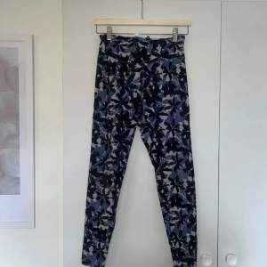 Säljer ett par snygga leggings med ett fint blommigt mönster i olika nyanser av blått, lilla och svart. Perfekta för både träning och vardagsbruk. De är stretchiga och bekväma, vilket gör dem till ett måste i garderoben!💕