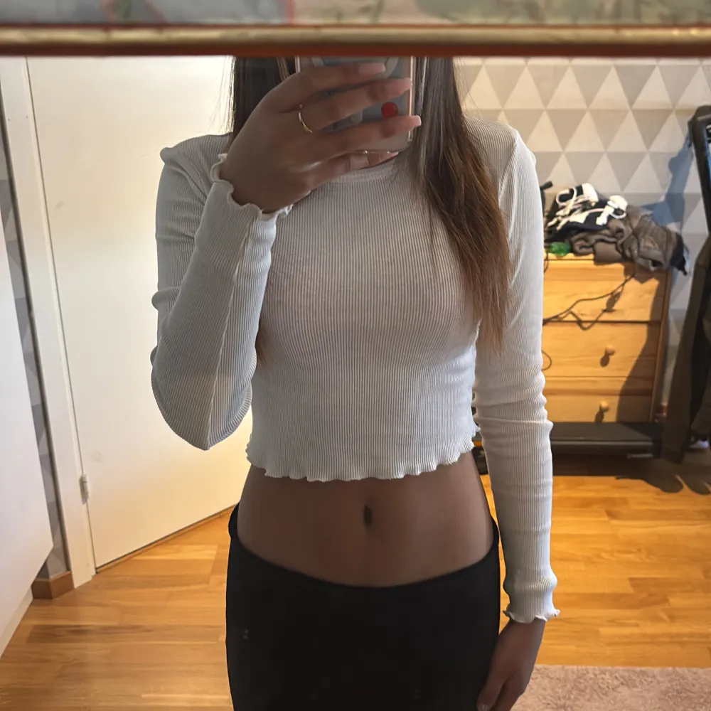 Säljer en superfin vit ribbad tröja med långa ärmar. Den är croppad och har en söt volangdetalj längst ner. Perfekt för både vardag och fest! Passar bra till jeans eller kjol för en avslappnad men stilren look.. Toppar.