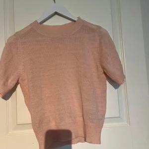 Ljusrosa stickad tröja - Säljer en söt ljusrosa stickad tröja med korta ärmar. Perfekt för vår och sommar! Tröjan har en enkel och stilren design som passar till det mesta. Den är mjuk och bekväm att ha på sig.