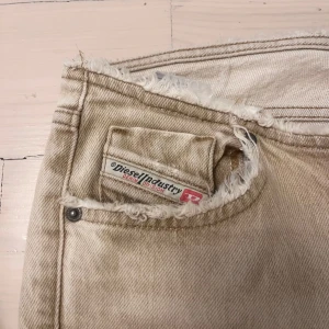 Diesel jeans - Supersnygga och coola jeans från Diesel i gul/beige färg som är lowwaist och bootcut. Har cool design med knapp på insidan! Har 2 defekter längst ner på byxan men inget som man ser när man har på sig jeansen! 