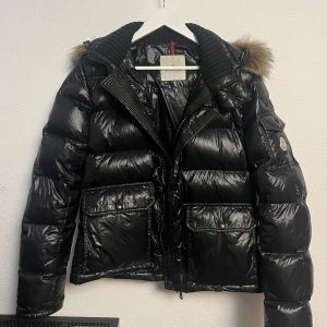 Moncler jacka - Säljer en snygg svart jacka från Moncler i hyfsat bra skick, förutom att cartoon delen inuti jackan har lossnat lite (den sitter fast i båda kanterna på övriga sidan av den). Annars är den perfekt för vintern och håller dig varm. Kom med bud. Om du undrar nåt mer är det bara och fråga. Mvh
