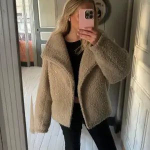 Supermysig beige teddyjacka som är perfekt för höst och vinter. Den har en oversized passform och långa ärmar, vilket gör den extra bekväm och varm. Jackan har en stilren design med knappar framtill. Perfekt för att hålla stilen när det blir kallare ute!