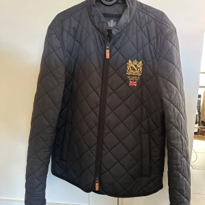 Marinblå quiltad jacka från Morris - Säljer en snygg svart quiltad jacka från Morris med broderad logga och brittisk flagga på bröstet. Jackan har en dragkedja framtill och är perfekt för höst och vår. Den är i mycket bra skick och passar både till vardags och lite finare tillfällen. Nypris 2199kr