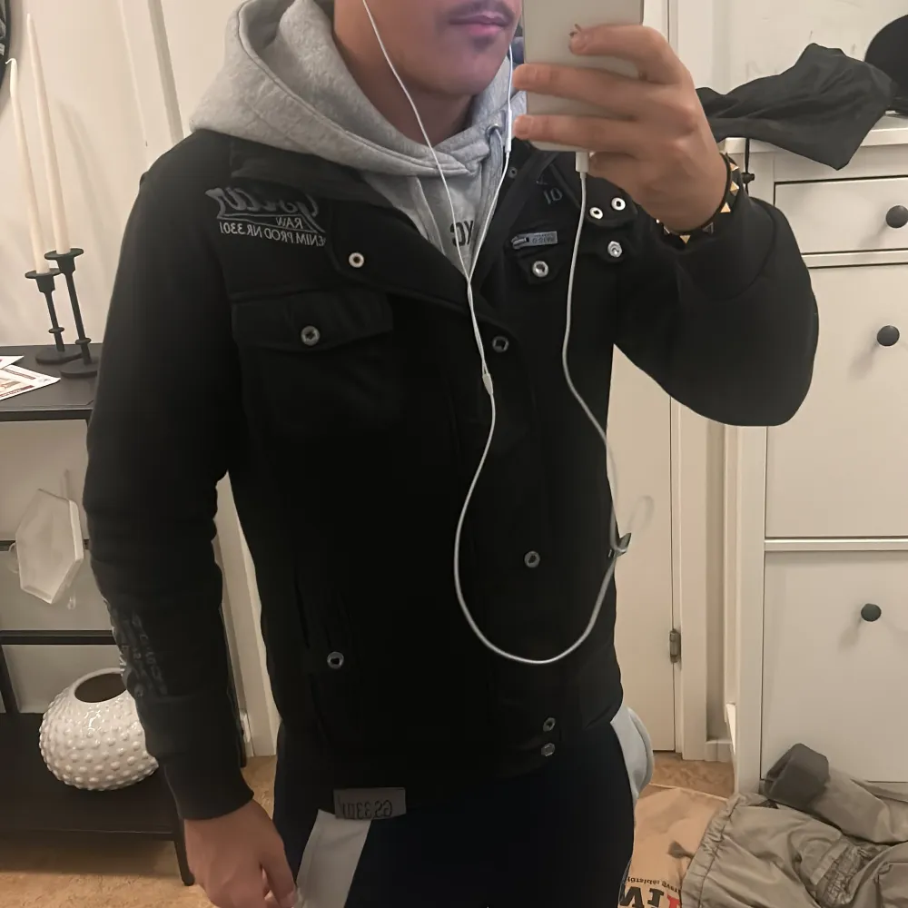 Säljer en snygg svart jacka från G-Star RAW i bra skick. Jackan har långa ärmar och knappar framtill. Perfekt för höst och vår, och den ger en cool look med sin broderade logga på bröstet. Passar perfekt för en casual stil eller en utekväll. Hör av dig vid intresse!. Jackor.