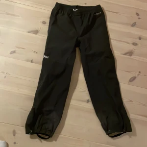 Svarta byxor från Helly Hansen - Säljer ett par svarta byxor från Helly Hansen i mycket bra skick. De är perfekta för utomhusaktiviteter med elastisk midja. Bra impregnering.