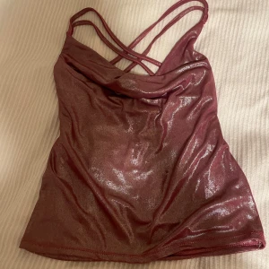 Glittrig lila topp med öppen rygg - Säljer en snygg lila topp med glittrigt material och öppen rygg. Den har dubbla axelband som korsas i ryggen för en extra cool look. Perfekt för fest eller en utekväll! ✨