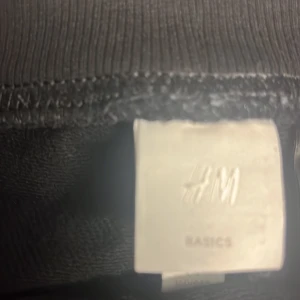 Svarta mjukisbyxor från H&M - Säljer ett par svarta mjukisbyxor från H&M Basics. De är superbekväma med en elastisk midja och snörning för perfekt passform. Perfekta för en chill dag hemma eller en snabb tur till affären. De har ribbade muddar vid bensluten för en snygg look. Passar till allt och är ett måste i garderoben!