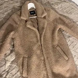 Säljer en supermysig beige teddyjacka från ONLY. Perfekt för kalla höst- och vinterdagar. Jackan har en klassisk krage och stängs med knappar. Den är långärmad och har en normal passform. 🤍