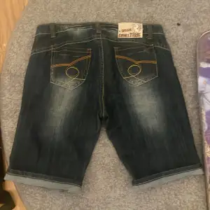 Säljer ett par mörkblå jeansshorts i mycket bra skick. De har en klassisk femficksdesign med snygga orangea sömmar på bakfickorna. De har bekväm passform. Färgen e en väldigt mörk blå ish grå skulle ja säga me as cool wash på dom