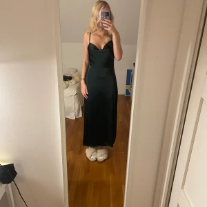Mörkgrön långklänning - Säljer en elegant mörkgrön långklänning med smala axelband och en vacker v-ringning. Klänningen har en stilren design och är perfekt för festliga tillfällen. Materialet ser ut att vara mjukt och följsamt, vilket ger en fin passform. 