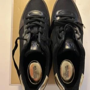 Svarta sneakers med gulddetaljer - Snygga svarta sneakers från Michael Kors med gulddetaljer på hälen. Perfekta för både vardag och festliga tillfällen. De är endast använda en gång!