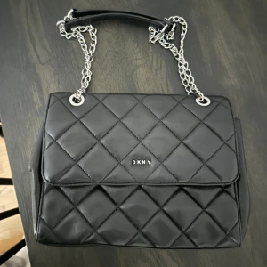 DKNY väska - Säljer min otroligt fina svarta 100% läderväska med silver kedja från DKNY.  Väskan köptes i USA inne i DKNY butik. Fint skick, försiktigt använt Dustbag tillkommer.