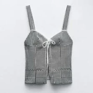 Svartvit rutig topp - Snygg svartvit rutig topp med smala axelband och knytning framtill. Perfekt för sommardagar eller en avslappnad fest. Den har en figurnära passform och är tillverkad i ett lätt och bekvämt material.