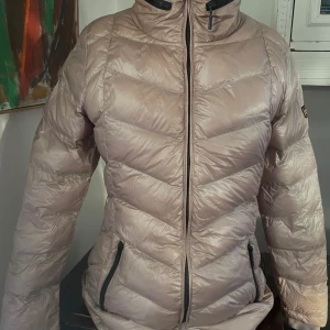 Beige fibredown jacka från Barbour International - Säljer en snygg beige fibre downjacka från Barbour International. Jackan har en quiltad design med dragkedja och hög krage för extra värme. Perfekt för kyliga dagar och har en stilren look. Den är i mycket bra skick och redo för nya äventyr!