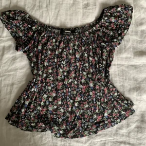 Blommig offshoulder topp från Bik Bok - Säljer en supersöt blommig offshoulder topp från Bik Bok i storlek XS. Den har ett härligt blommönster i rosa, blått och grönt på en svart bakgrund. Perfekt för sommardagar eller en mysig vårkväll. Toppen är i mycket bra skick och redo för nya äventyr! 🌸