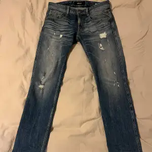 Säljer ett par snygga blå jeans från Replay i modellen Anbass. De har en cool slitningseffekt och är i perfekt skick. Perfekta för en avslappnad stil. Jeansen har en perfekt “fade” och unika slitningar. Hör av dig vid minsta fundering. 