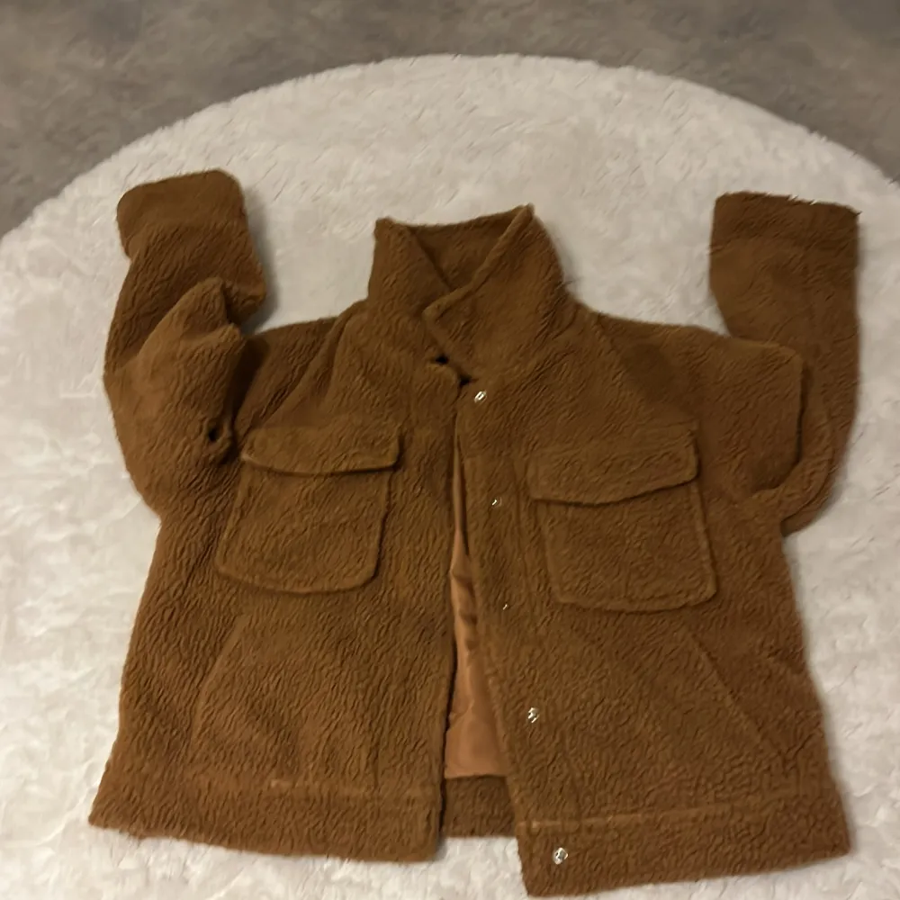 Mysig brun teddyjacka från Gina Tricot i storlek 40. Perfekt för kyliga dagar med sin fluffiga och varma design. Jackan har långa ärmar och praktiska fickor framtill. Stängs med knappar för en stilren look. Passar perfekt till höst och vinter!. Jackor.