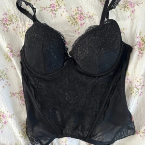 Svart spetskorsett - Snygg svart korsett med spetsdetaljer och justerbara axelband. Från Ella M, i storlek 80C