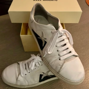 Vita sneakers från Axel Arigato - Säljer ett par vita sneakers från Axel Arigato i bra skick. Skorna har en snygg fågeldetalj i svart på sidan och klassisk snörning. Storlek 41 med originalförpackning och dustbag.