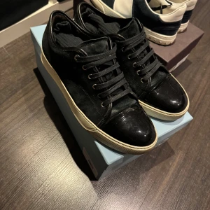 Lanvin cap toe - Snygga svarta sneakers från Lanvin med snörning och en stilren design. Skorna har en blank finish på tån och en vit sula som ger en cool kontrast. Perfekta för en trendig look.