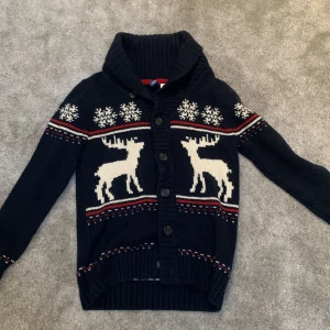 Mörkblå stickad kofta med renmotiv från  - Mysig svart stickad kofta från H&M med vita renar och snöflingor. Koftan har en ribbad krage och knappar framtill. Perfekt för kyliga dagar! Väldigt trendigt just nu. Den säljs inte längre. Pris kan diskuteras!