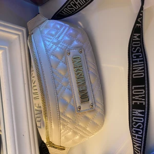 Vit quiltad axelväska från Love Moschino - Snygg vit quiltad axelväska från Love Moschino med guldfärgad dragkedja och justerbar axelrem. Perfekt för att ge din outfit en lyxig touch. Väskan har ett stilrent märke framtill och rymligt inre för dina nödvändigheter.Köptes för 1245 kr på Zalando, men inte kommit till användning tyvärr
