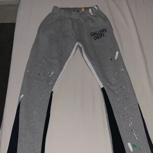 Grå mjukisbyxor från Gallery Dept. - Snygga grå mjukisbyxor från Gallery Dept. med coola färgstänk och elastisk midja. Tillverkade i 100% bomull för en bekväm känsla. Perfekta för en avslappnad stil med en unik touch.