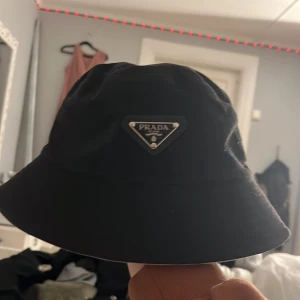 Svart hatt från Prada - Snygg svart hatt från Prada med en klassisk design. Hatten har en diskret logotyp framtill och är perfekt för en stilren look. Den är bekväm och passar till alla klädstilar, Jag köpte den för 6 292 kronor och nu säljer jag den för 3 000 hälften av priset men skriv privat om du är snabb får du den billigare , och den är som ny🫶🏼