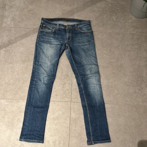 Nudie Jeans - Snygga blå jeans från Nudie Jeans med klassisk femficksdesign och orange sömmar. Jeansen har en slim passform och är perfekta för en avslappnad stil. 