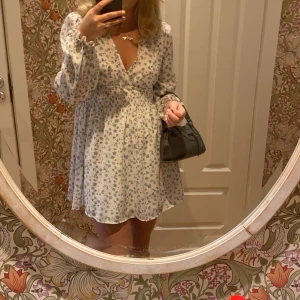 Blommig klänning från Lager 157 - Söt blommig klänning från Lager 156 i ljusa färger. Den har en v-ringad design med långa ärmar och ett elastiskt midjeband för en bekväm passform. Perfekt för vår och sommar!