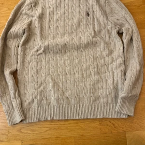 Beige kabelstickad tröja från Ralph Lauren - Säljer en stilren beige kabelstickad tröja från Ralph Lauren. Tröjan har långa ärmar och en klassisk rund halsringning. Perfekt för kyligare dagar och ger en tidlös look.