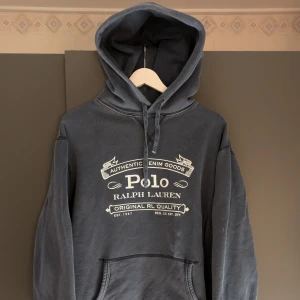 Mörkblå hoodie från Ralph Lauren - Säljer en snygg mörkblå hoodie från Ralph Lauren med tryck på framsidan. Den har en klassisk känguruficka och justerbar huva med snören. Perfekt för en avslappnad stil. 