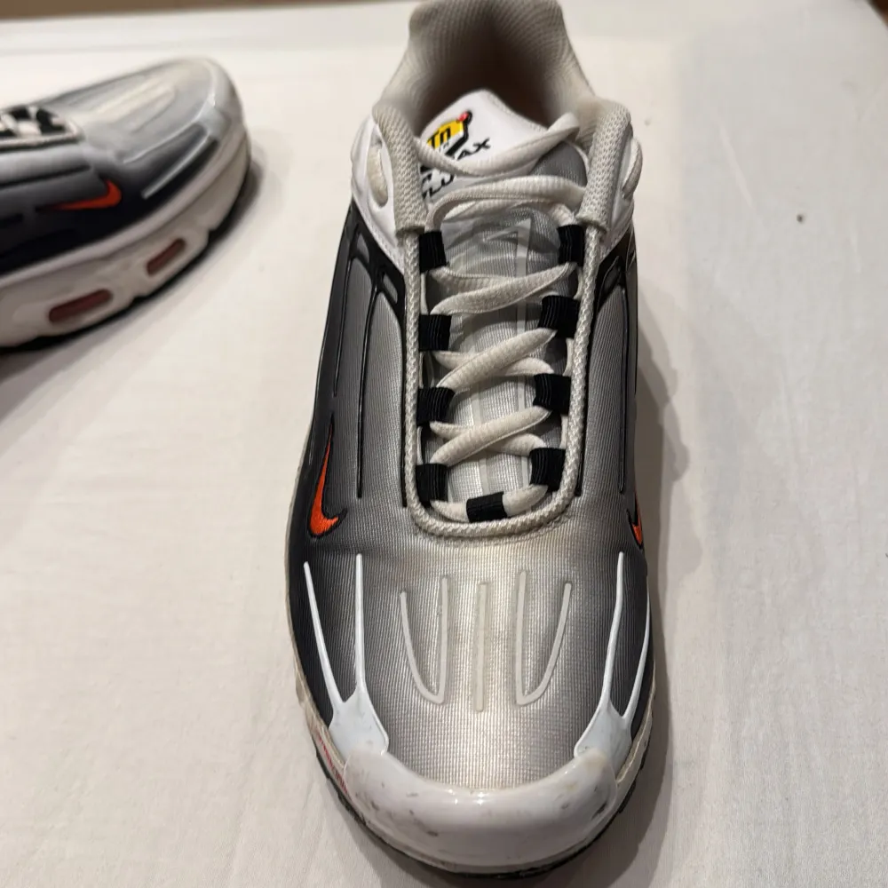 Snygga Nike Air Max sneakers i silver med svarta och röda detaljer. Skorna har en futuristisk design med synlig dämpning i sulan och klassisk snörning. Perfekta för en sportig look.. Kengät.