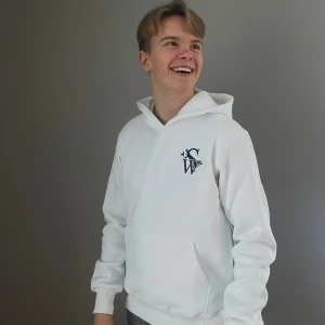 Vit hoodie med logotyp - Säljer en stilren vit hoodie med en svart logotyp på bröstet. Hoodien har en klassisk design med känguruficka och justerbar huva. Perfekt för en avslappnad look.